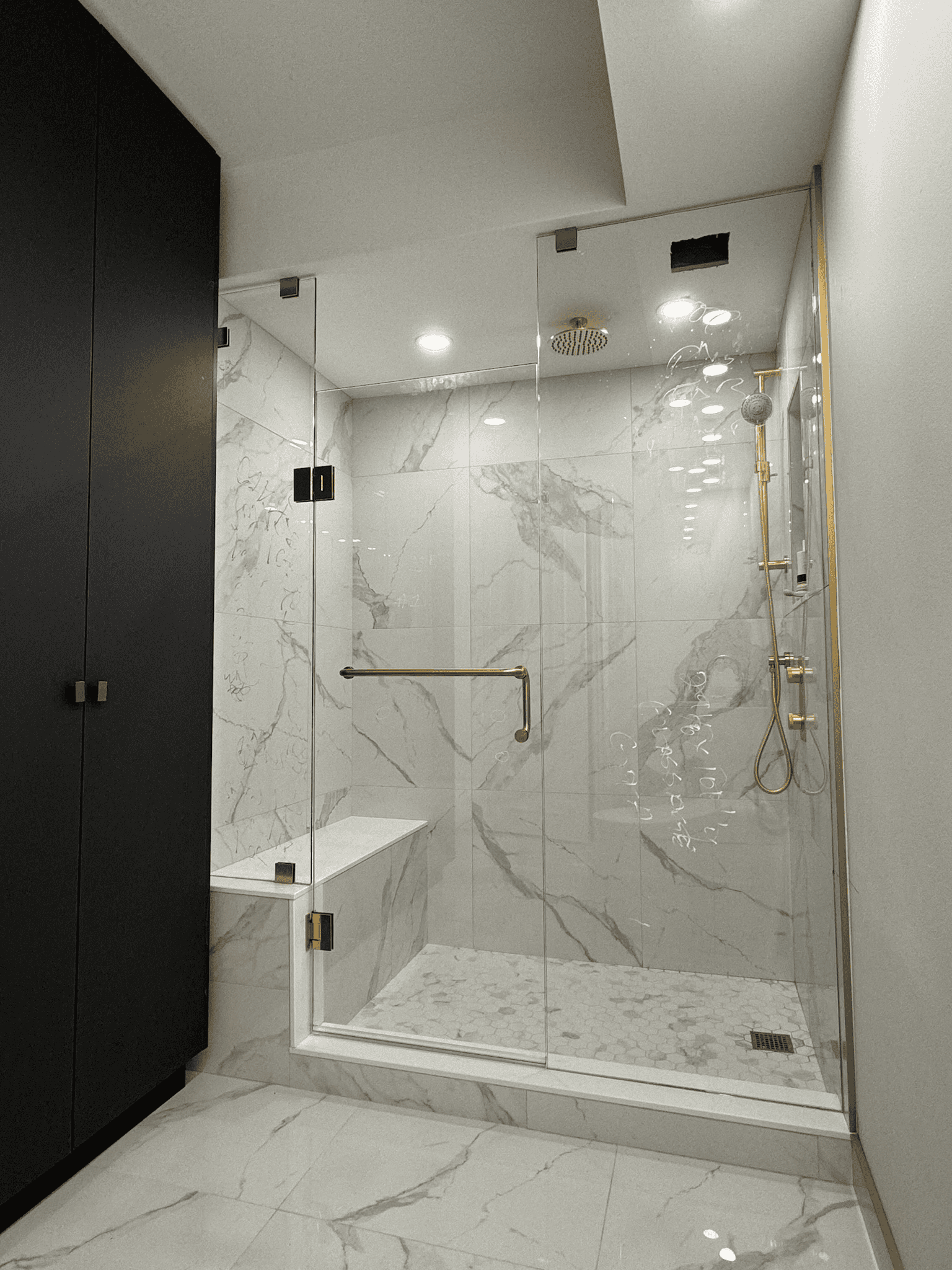 Frameless glass shower with brushed gold hardware and a built-in bench, installed in Innisfil — a modern spa-style upgrade by Zelux Railings.