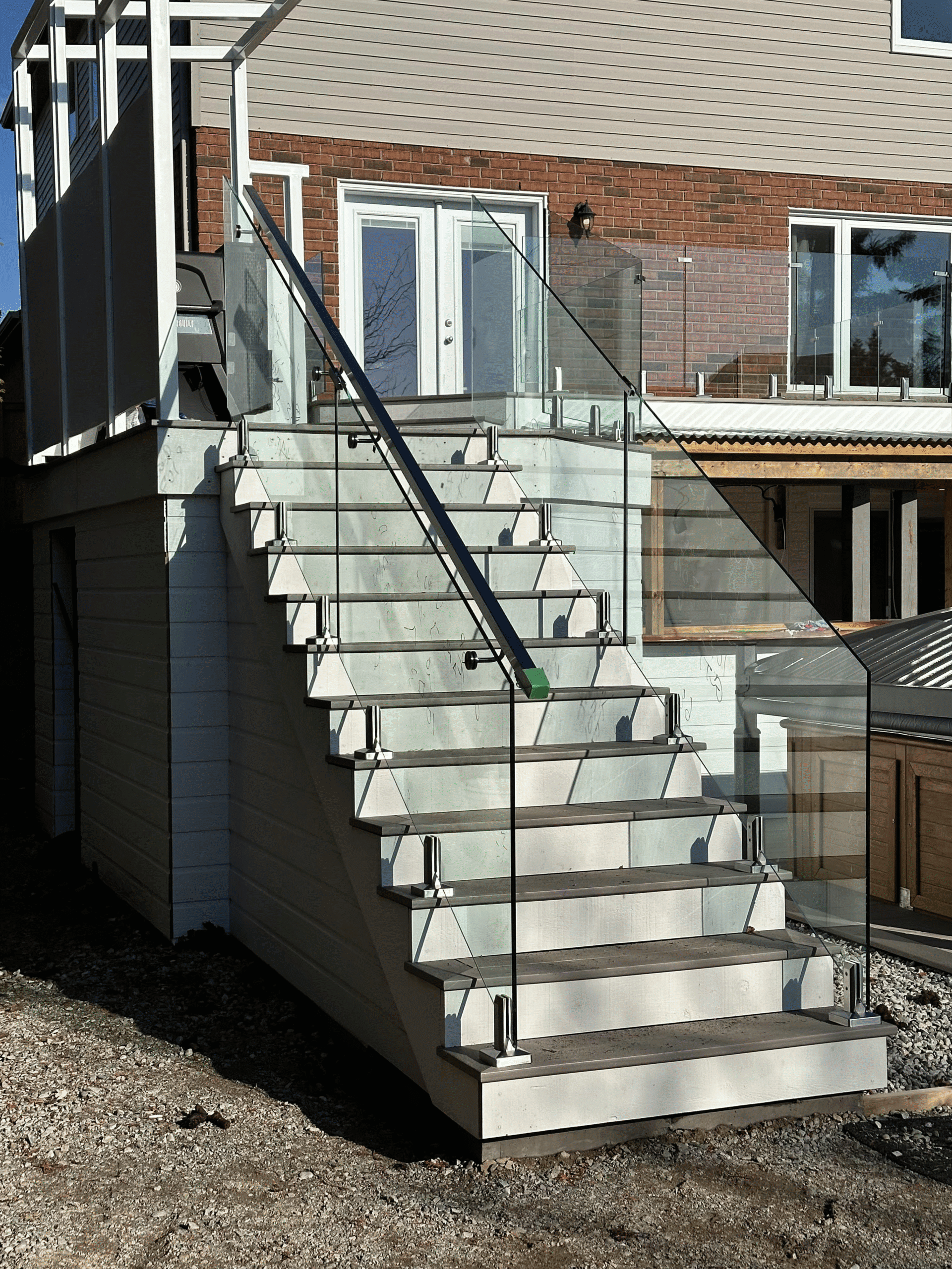 Outdoor stair railing with frameless glass panels by Zelux Railings – custom deck installation with stainless steel clamps and minimalist handrail.